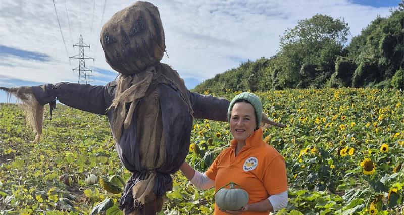 Caroline Harriott beside a scarecrow in a field of sunflowers