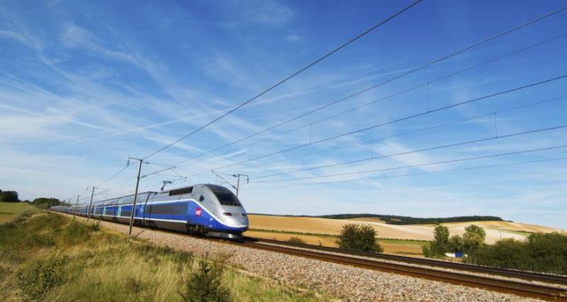 A picture of a high speed train going through the countryside on a sunny day.